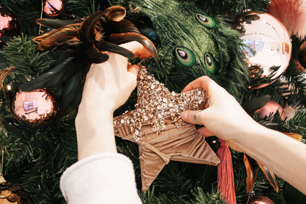 Hands add a large star decoration to a Christmas tree