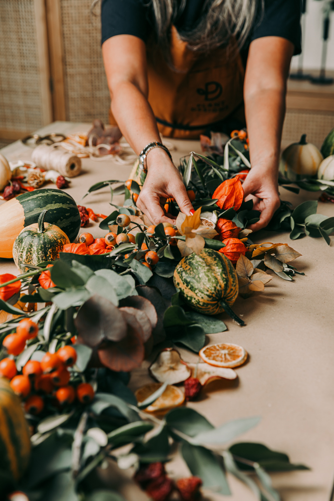 Hands making a foliage garland at a workshop table
