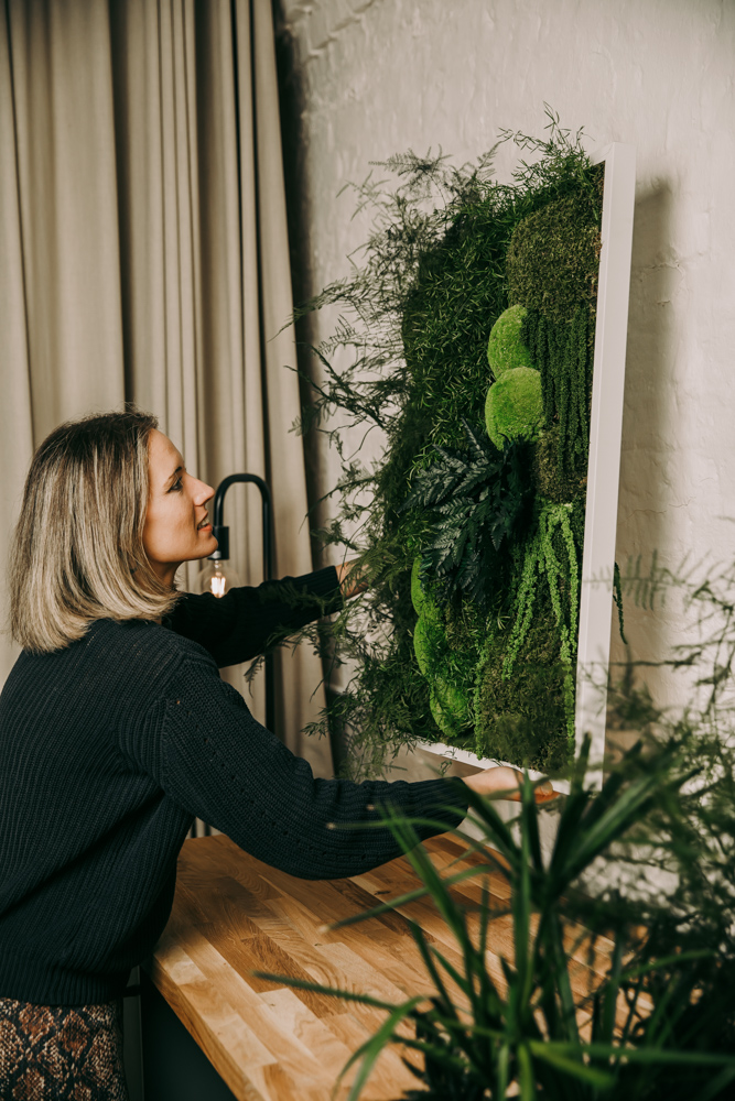 A person placing a moss frame on a wall with preserved planting in front